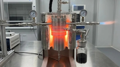 Glowing laboratory reactor at high temperature with pressure gauges and a jar of black carbon powder nearby