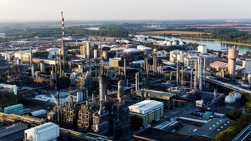 Drone shot of an expansive petrochemical refinery with tall stacks and processing columns near a wide river